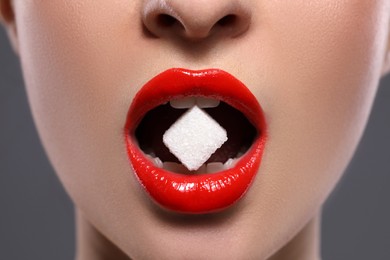 Photo of Closeup view of young with beautiful lips eating sugar cube on grey background