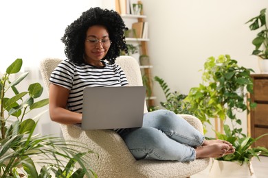 Relaxing atmosphere. Woman with laptop sitting on armchair surrounded by houseplants at home