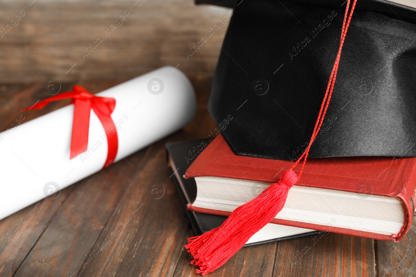 Photo of Graduation hat, books and student's diploma on wooden table, closeup