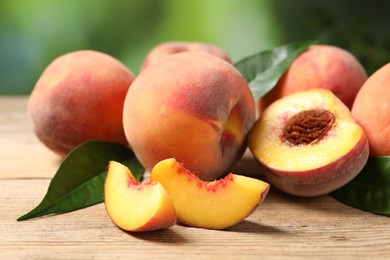 Photo of Cut and whole fresh ripe peaches with green leaves on wooden table against blurred background, closeup
