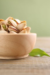Tasty pistachios in bowl on wooden table against olive background, closeup
