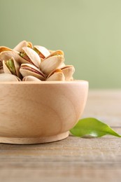 Photo of Tasty pistachios in bowl on wooden table against olive background, closeup