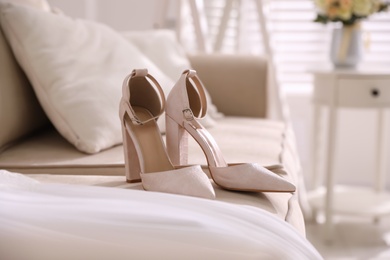 Photo of Elegant high heeled shoes and wedding dress on sofa indoors