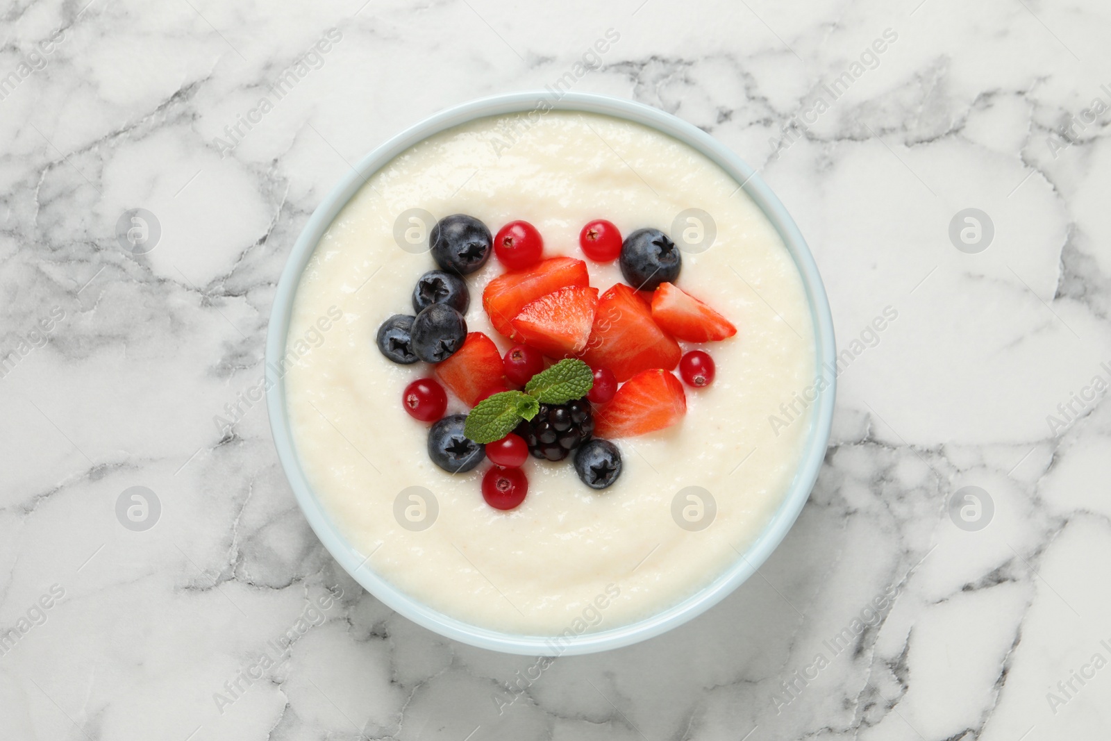 Photo of Delicious semolina pudding with berries on white marble table, top view