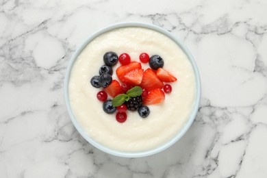 Photo of Delicious semolina pudding with berries on white marble table, top view