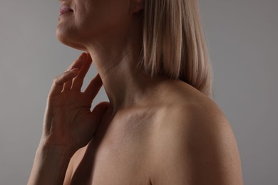 Woman touching her neck on grey background, closeup