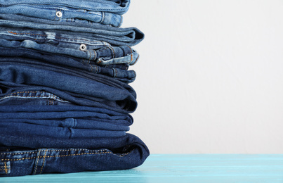 Photo of Stack of different jeans on blue wooden table. Space for text