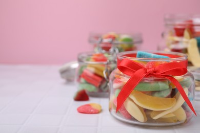 Photo of Glass jars with tasty colorful jelly candies on white tiled table against pink background. Space for text