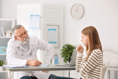 Coughing teenage girl visiting doctor at clinic