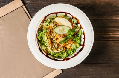 Photo of Plate with delicious fresh salad and menu on table, top view