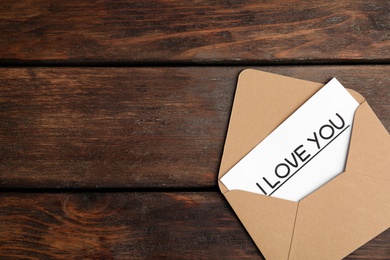 Photo of Card with phrase I Love You in envelope on wooden table, top view. Space for text