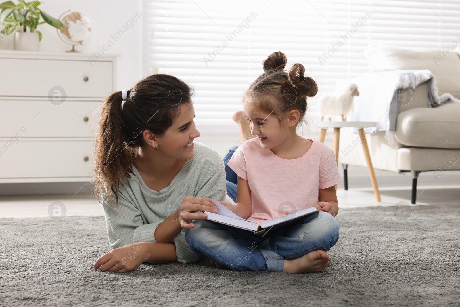 Photo of Young mother and her daughter reading book on floor at home