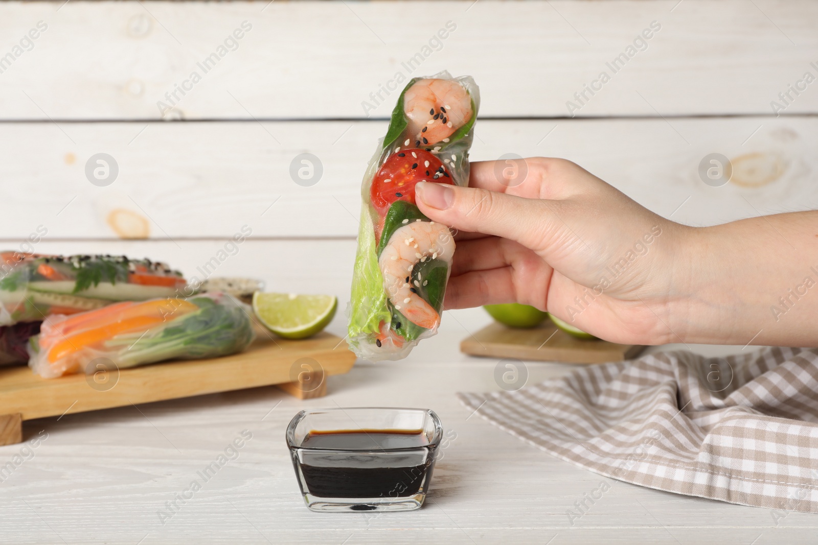 Photo of Woman dipping roll wrapped in rice paper into sauce at white wooden table, closeup