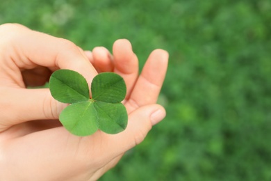 Photo of Woman holding four-leaf clover outdoors, closeup with space for text