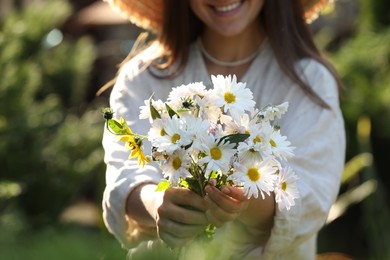 Photo of Woman holding bouquet of beautiful white chamomile flowers outdoors, closeup