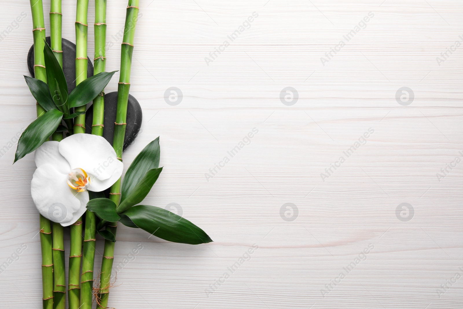 Photo of Spa stones, bamboo and orchid flower on light wooden table, flat lay. Space for text