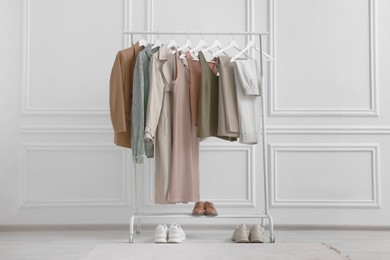 Photo of Rack with different stylish women`s clothes and shoes near white wall indoors