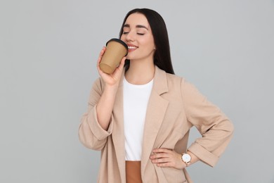 Young female intern with cup of drink on grey background