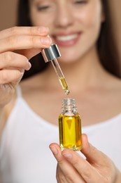 Woman with essential oil on brown background, selective focus