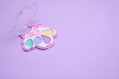 Photo of Children's eye shadow palette with brush on violet background, top view. Space for text