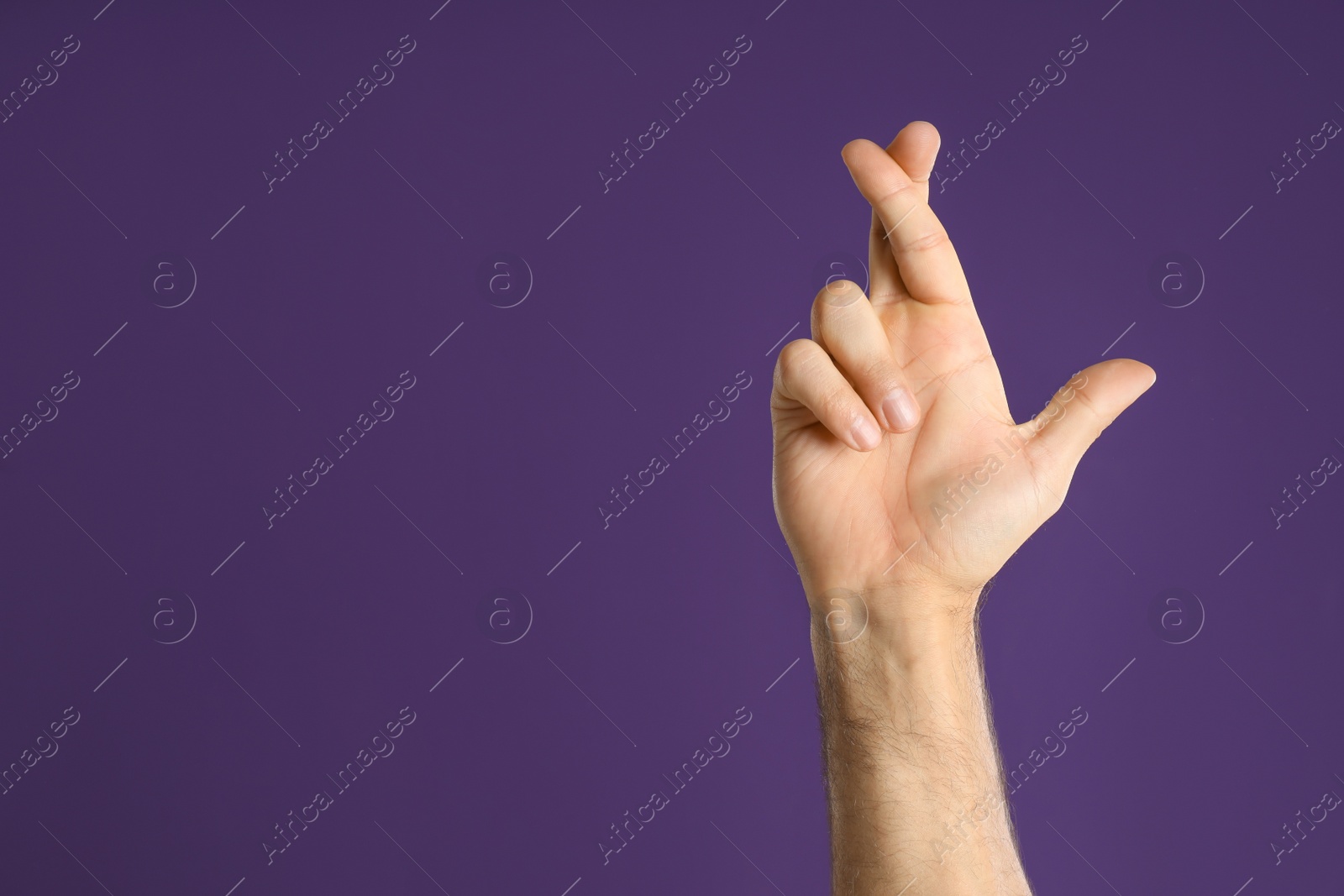 Photo of Man with crossed fingers and space for text on purple background, closeup. Superstition concept