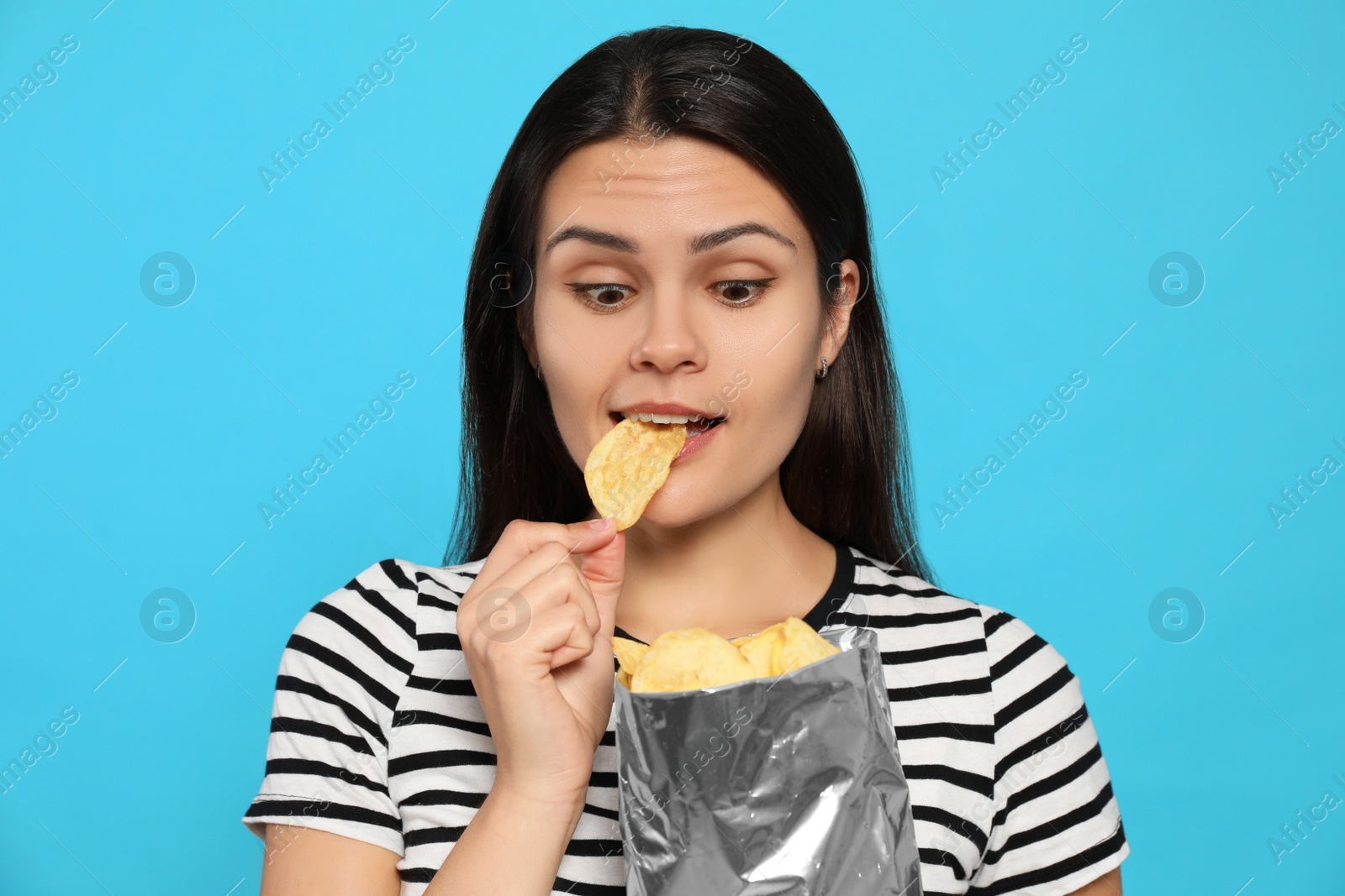 Photo of Beautiful woman eating potato chips on light blue background