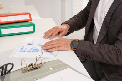 Photo of Businessman putting document into punched pocket at white table in office, closeup