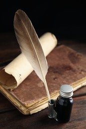 Photo of Feather pen, bottle of ink, old book and parchment scroll on wooden table