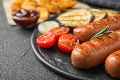 Delicious grilled sausages and vegetables on black table. Barbecue food