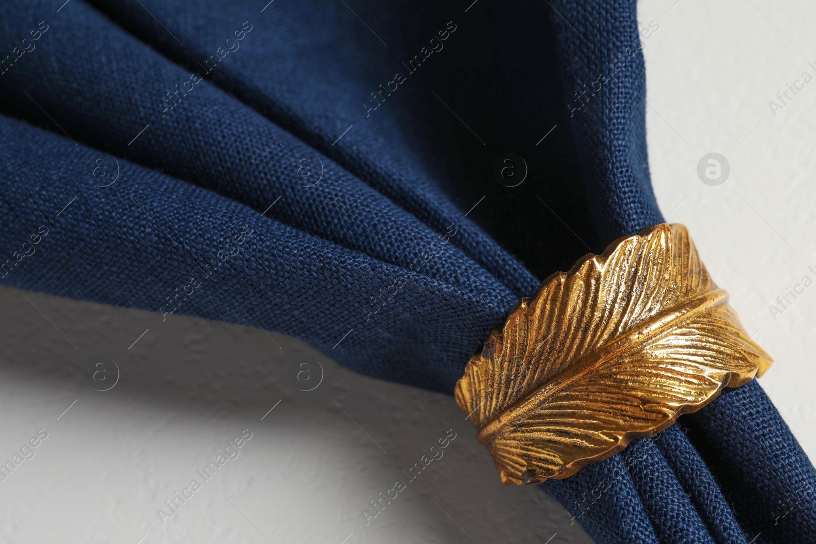 Photo of Dark blue fabric napkin and decorative ring for table setting on plate, closeup