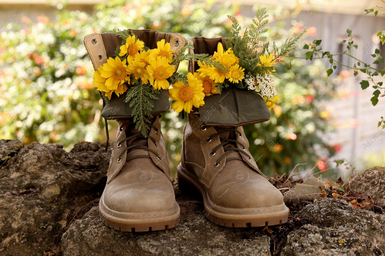 Photo of Boots with beautiful yellow flowers on stone outdoors