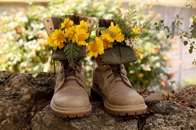 Boots with beautiful yellow flowers on stone outdoors