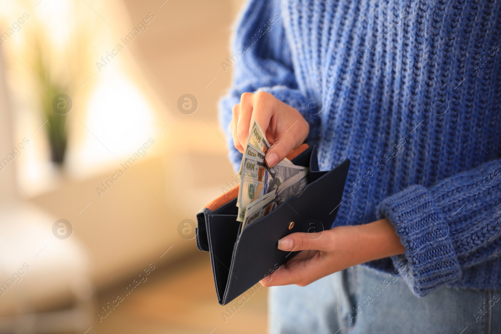 Photo of Young woman holding wallet with dollar bills on blurred background, closeup