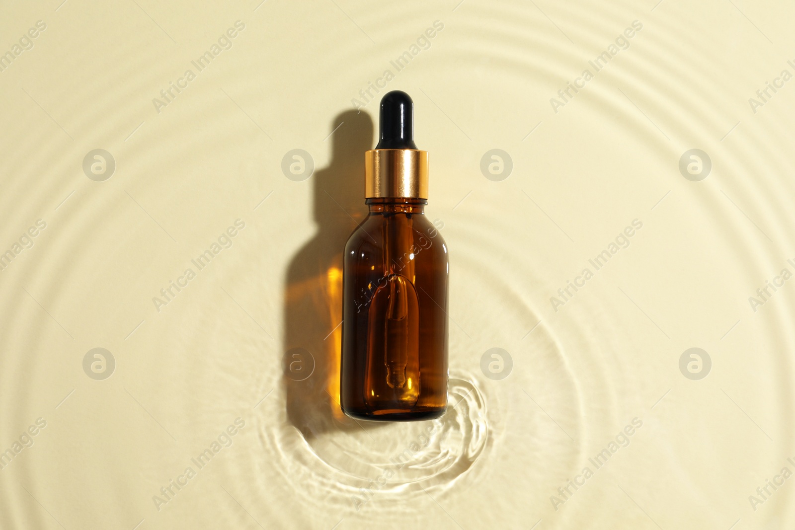 Photo of Bottle of cosmetic oil in water on beige background, top view