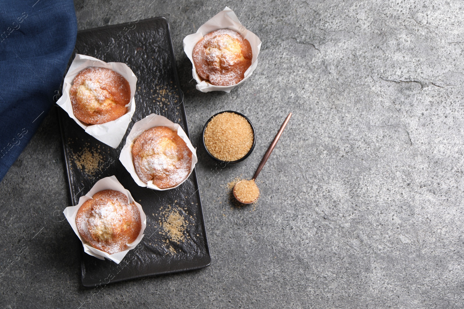 Photo of Delicious muffins and sugar on grey table, flat lay. Space for text