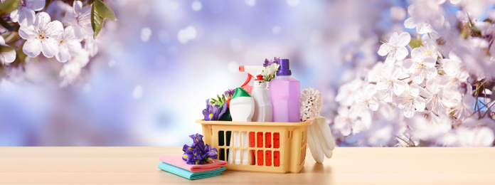 Image of Plastic basket with different detergents on wooden table. Spring cleaning concept 