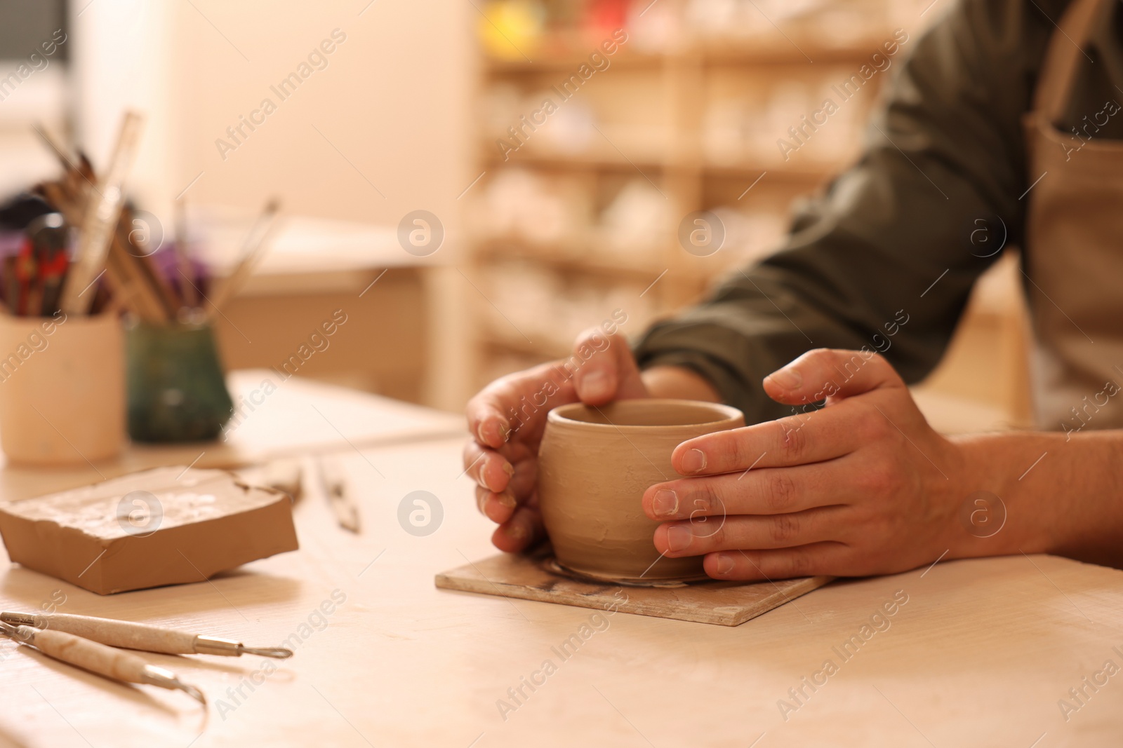 Photo of Clay crafting. Man making bowl at table indoors, closeup