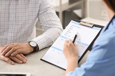 Photo of Doctor showing medical card to patient at table in clinic, closeup