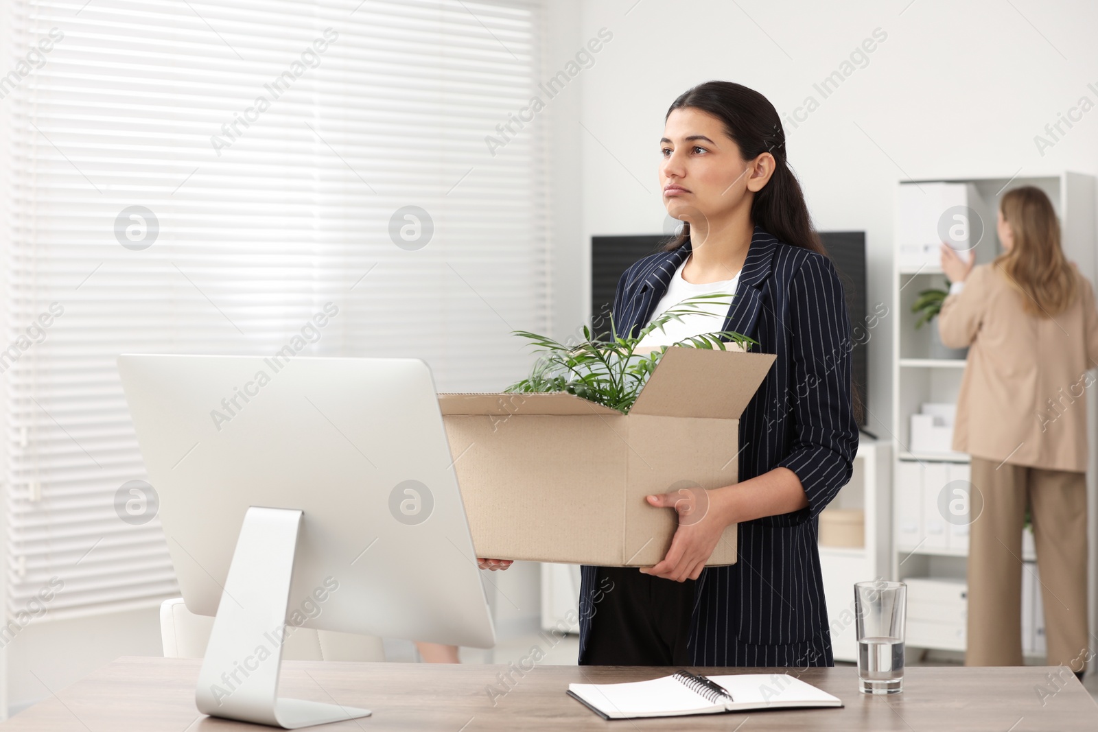 Photo of Unemployment problem. Woman with box of personal belongings at table in office