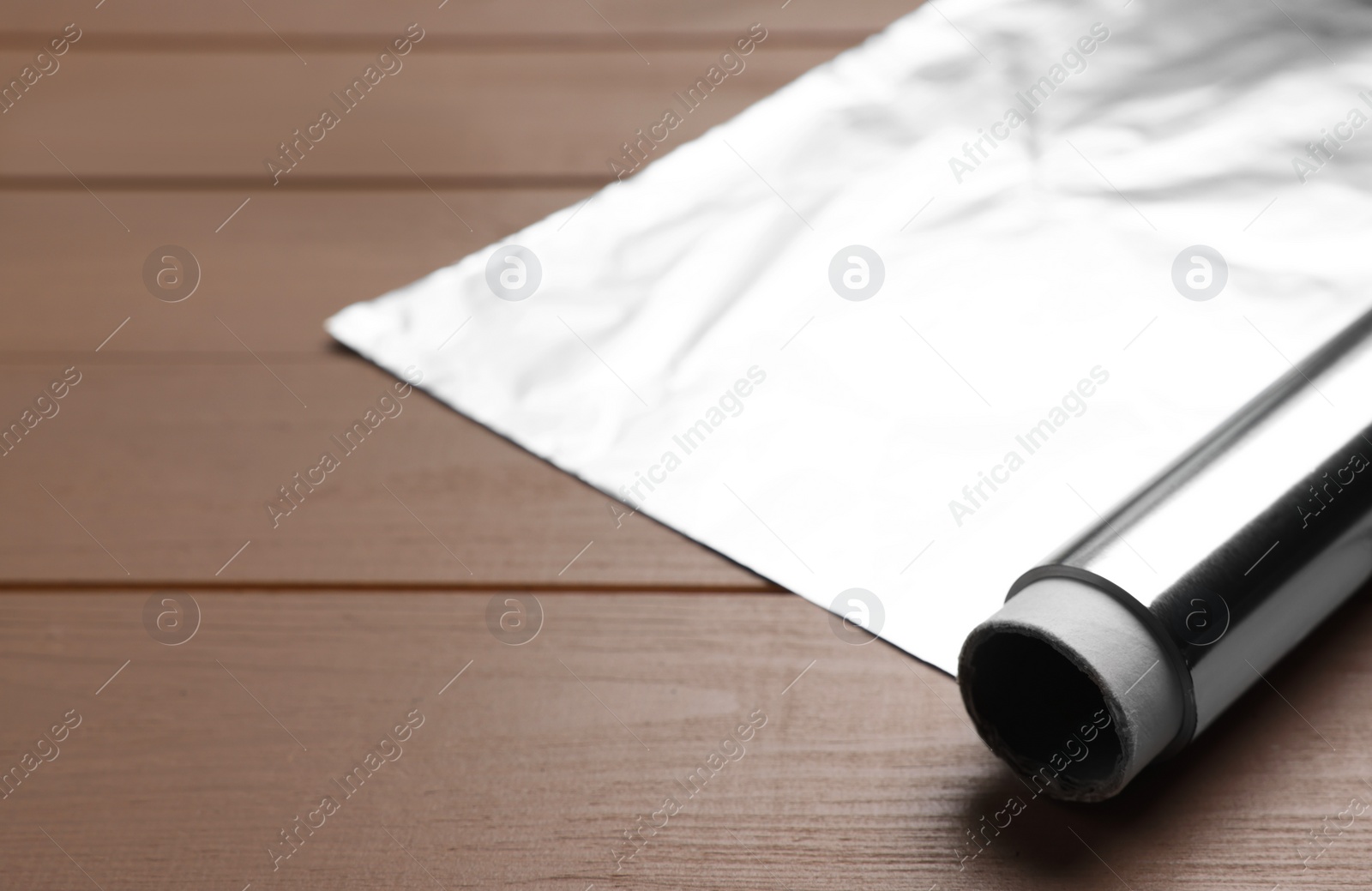 Photo of Roll of aluminum foil on wooden table, closeup. Space for text