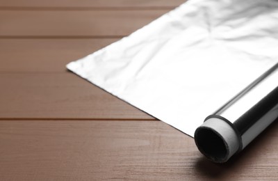 Photo of Roll of aluminum foil on wooden table, closeup. Space for text