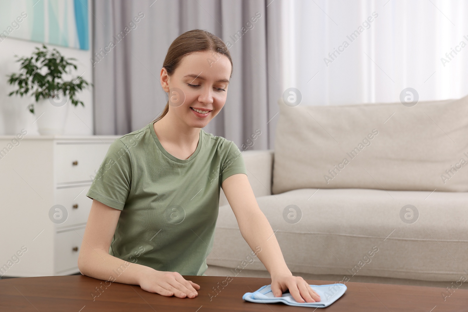 Photo of Woman with microfiber cloth cleaning wooden table in room
