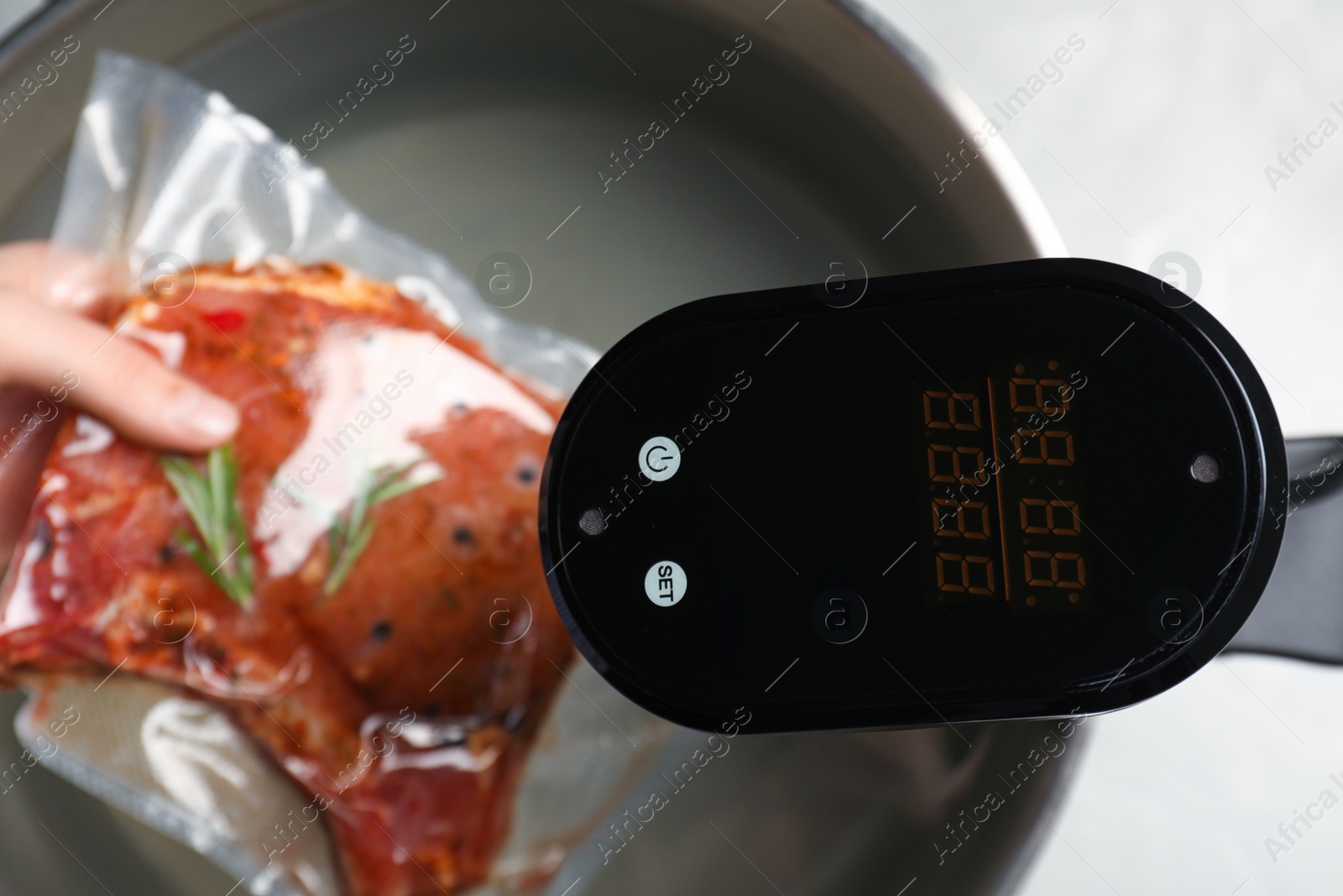 Photo of Woman putting vacuum packed meat into pot with thermal immersion circulator, closeup. Sous vide cooking