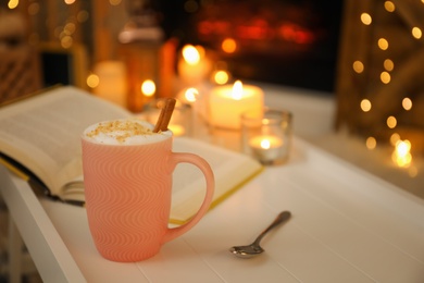 Photo of Cup of cocoa, spoon and book on white table indoors