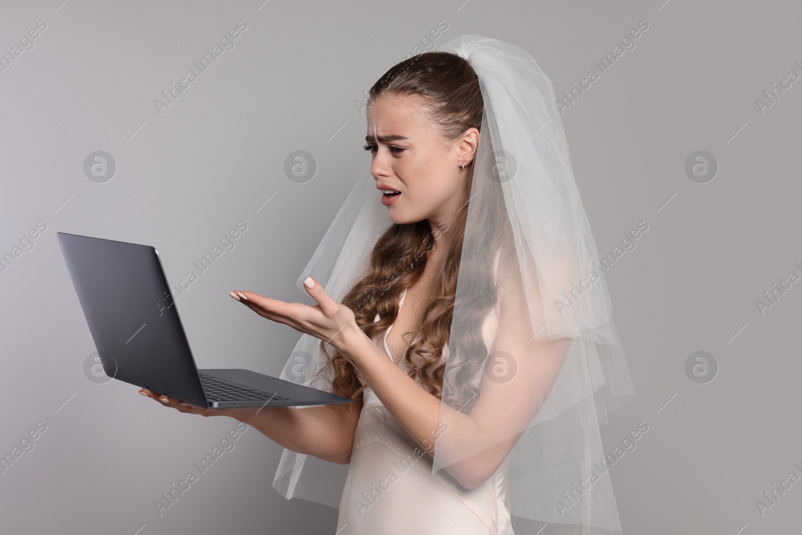 Photo of Shocked bride with laptop on gray background