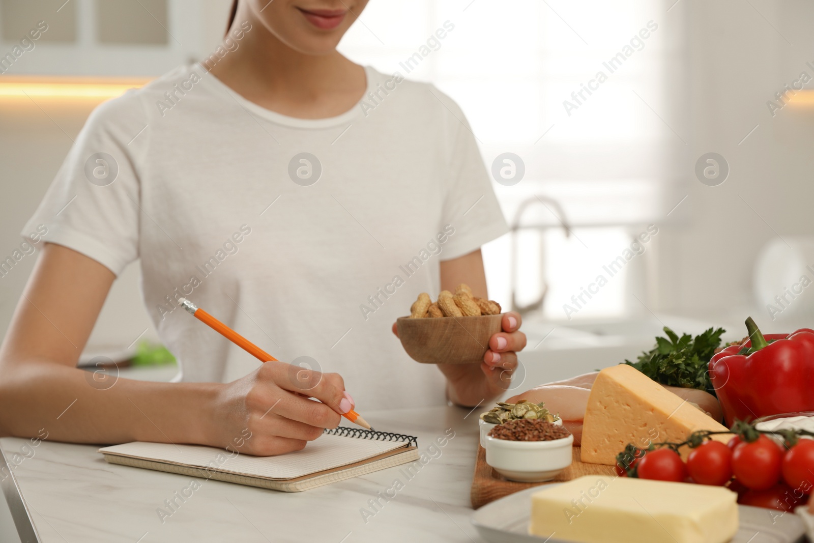 Photo of Woman writing in notebook near products at table, closeup. Keto diet