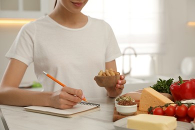 Photo of Woman writing in notebook near products at table, closeup. Keto diet