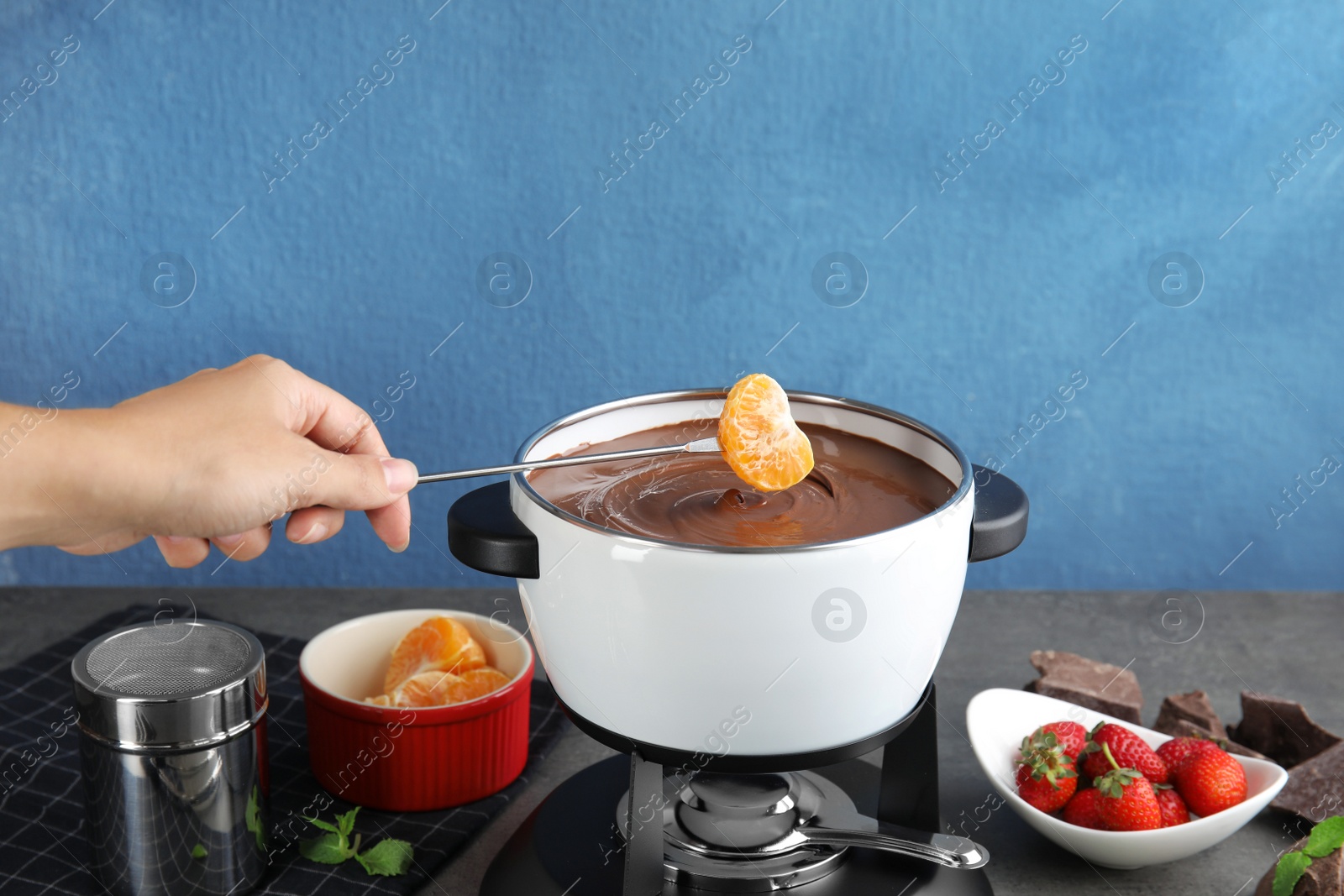 Photo of Woman dipping tangerine into pot with chocolate fondue on table, closeup