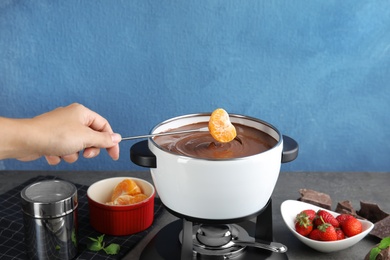 Woman dipping tangerine into pot with chocolate fondue on table, closeup