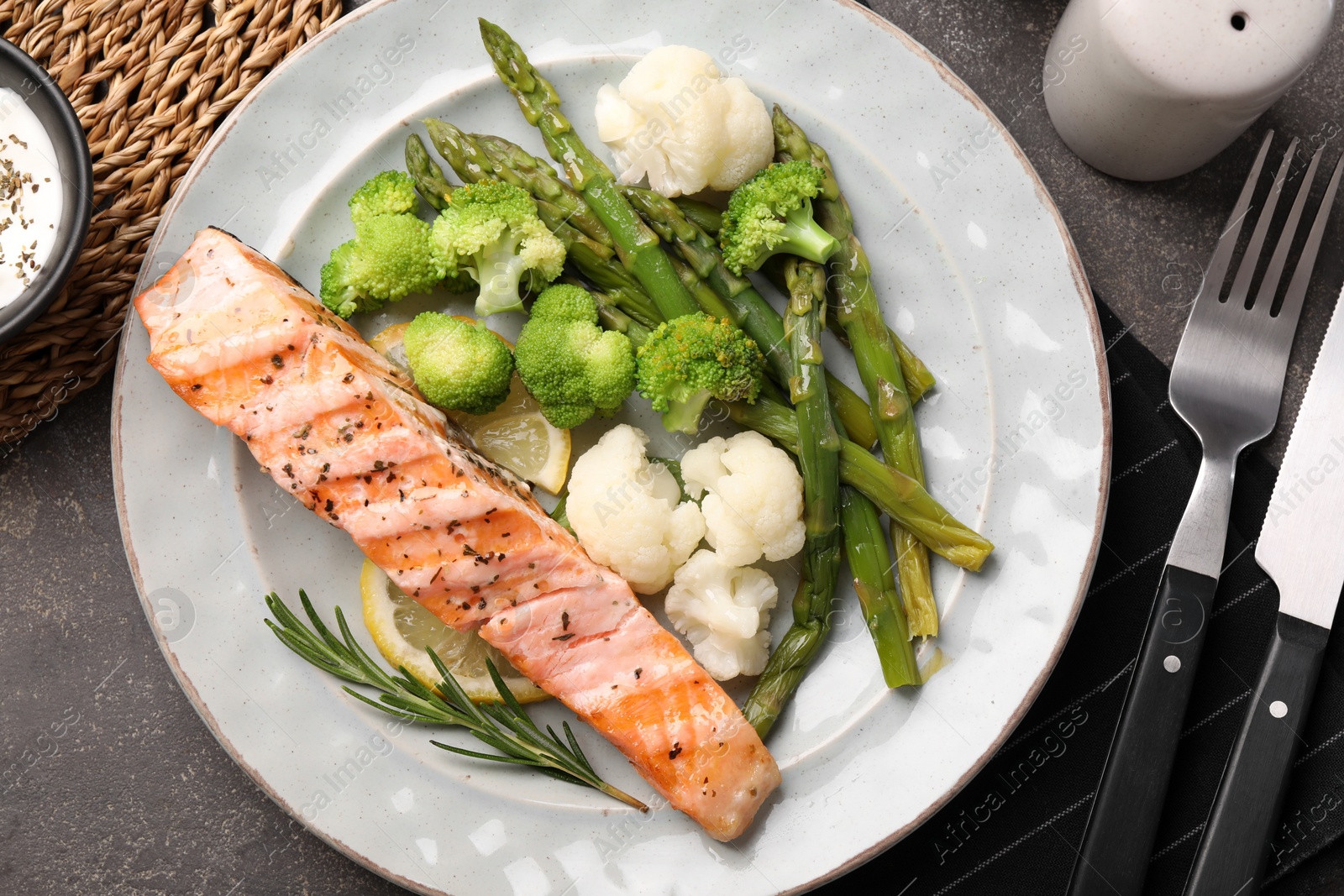 Photo of Healthy meal. Piece of grilled salmon, vegetables, asparagus and rosemary served on grey textured table, flat lay